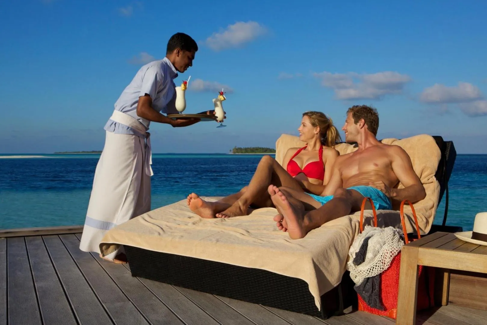 Un serveur apporte des boissons à un couple relaxant sur des transats en bord de mer.