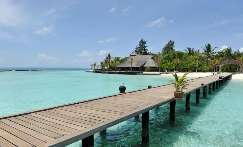 Un ponton en bois s'avance sur une eau turquoise vers des bungalows sur pilotis.