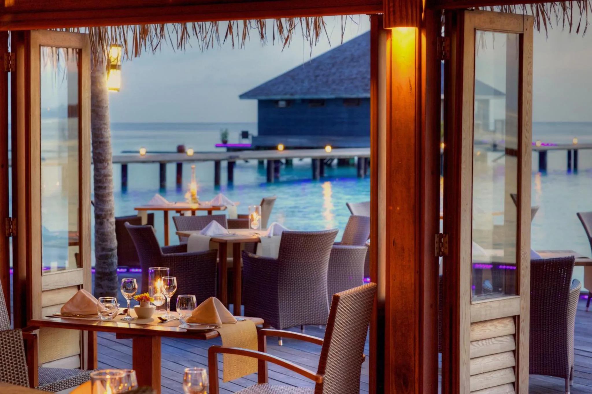 Une table est dressée sur une terrasse en bois avec vue sur la mer.
