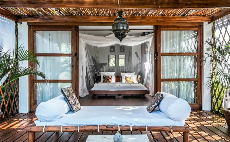 Espace de détente extérieur avec canapés et vue sur une chambre à moustiquaire.