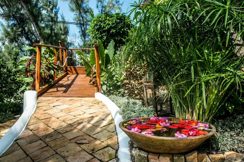 Un pont en bois traverse un jardin luxuriant avec une fontaine ornée de fleurs.