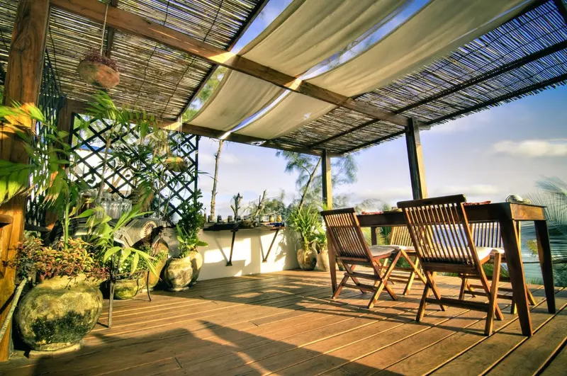 Terrasse en bois ombragée avec mobilier de jardin et végétation luxuriante.