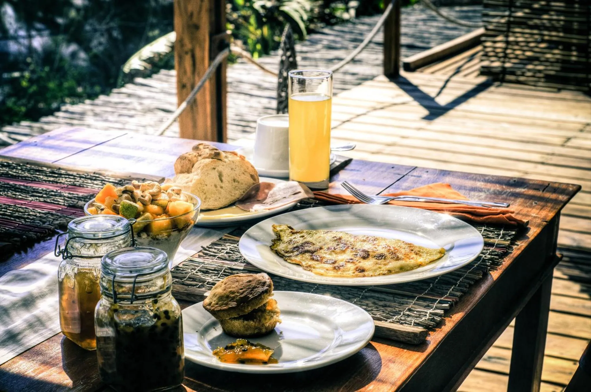 Une table en bois présente un petit-déjeuner avec des fruits, du pain et une omelette.