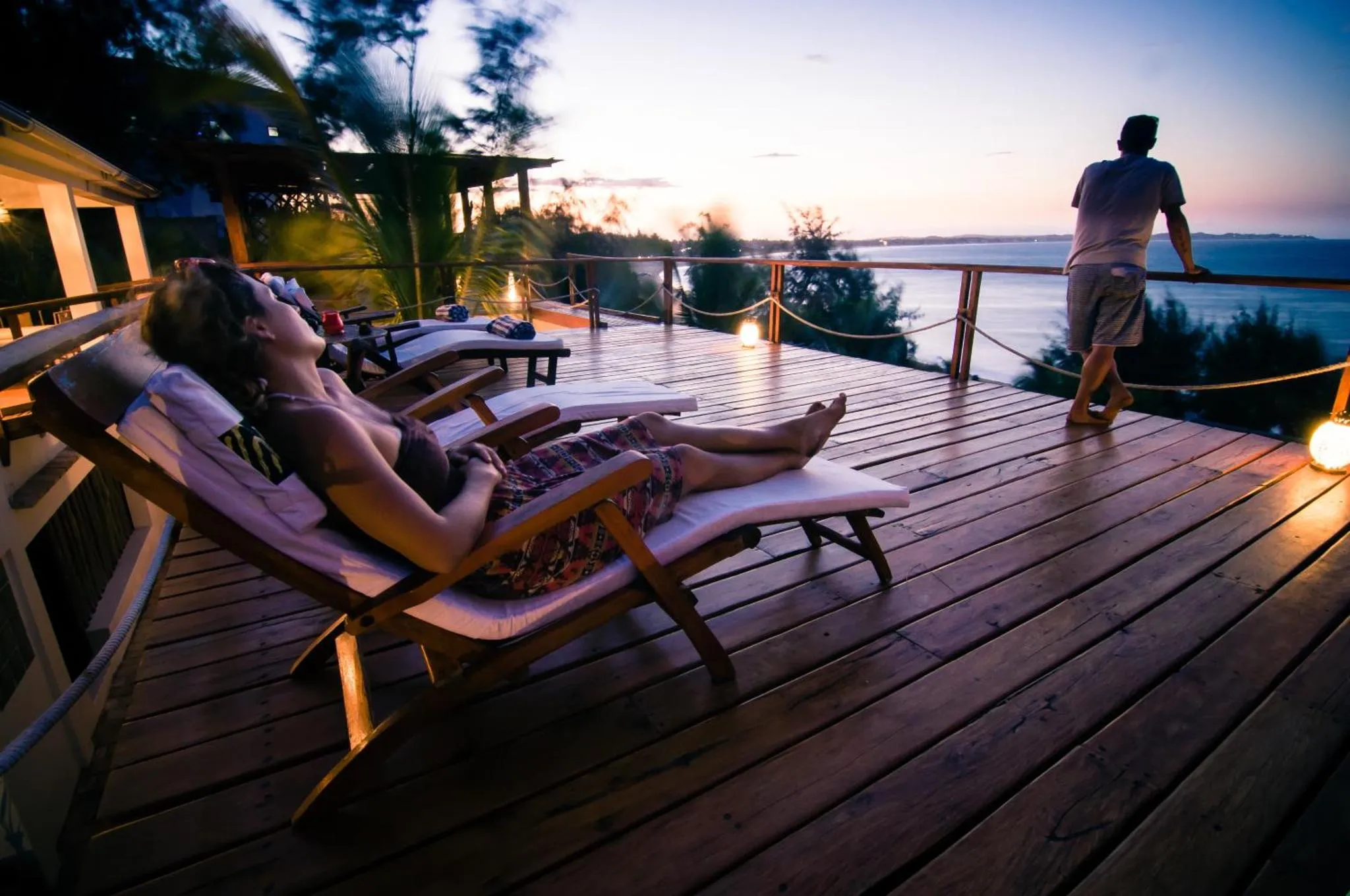 Des personnes se détendent sur une terrasse en bois au coucher du soleil.
