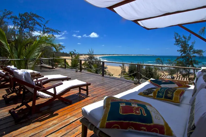Terrasse en bois avec chaises longues donnant sur une plage de sable.
