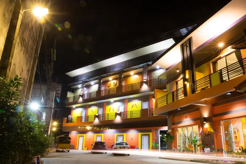 Façade d'un bâtiment illuminé la nuit avec des balcons et des véhicules garés devant.