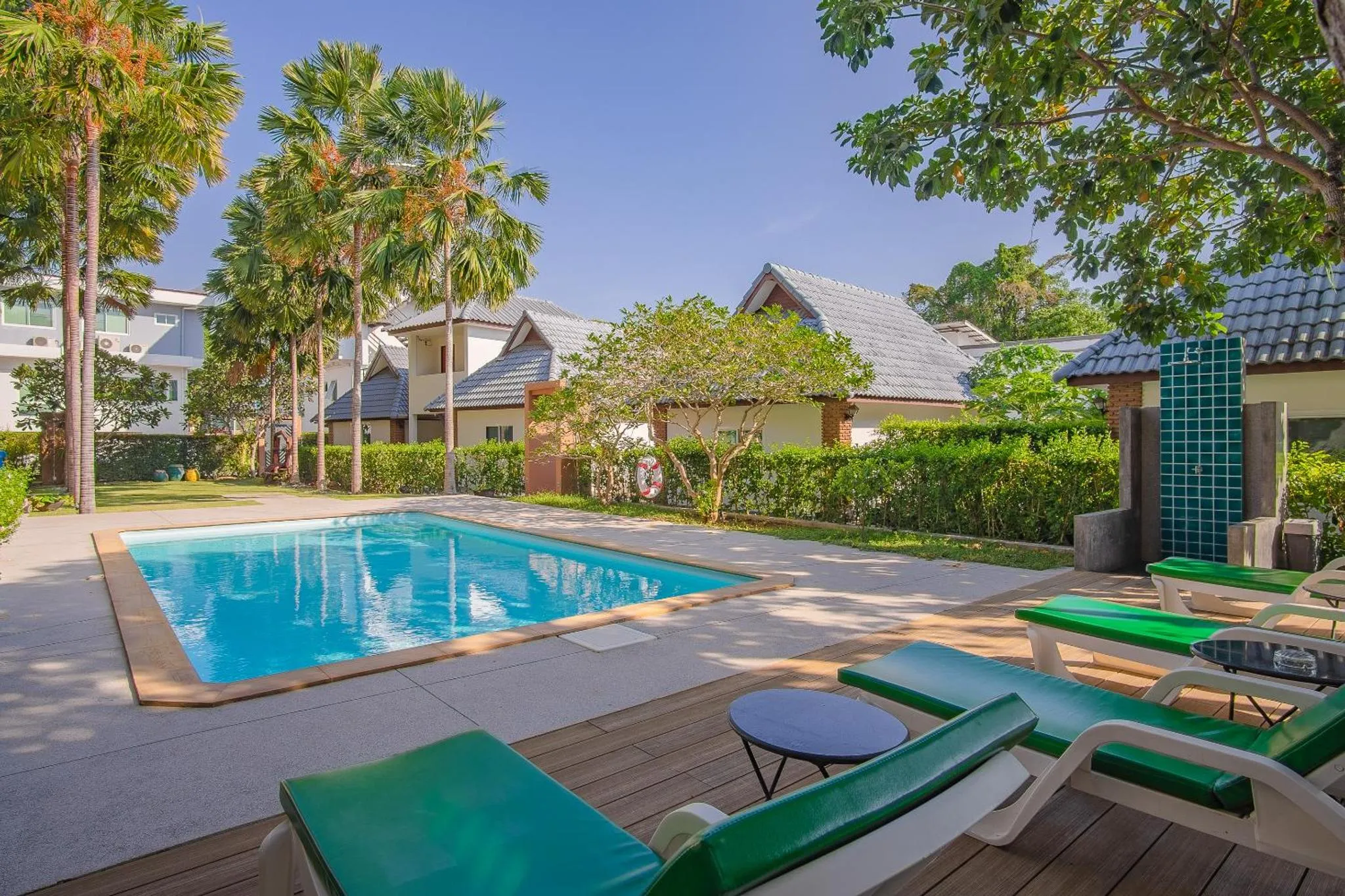 Transats verts disposés autour d'une piscine rectangulaire dans un jardin tropical.