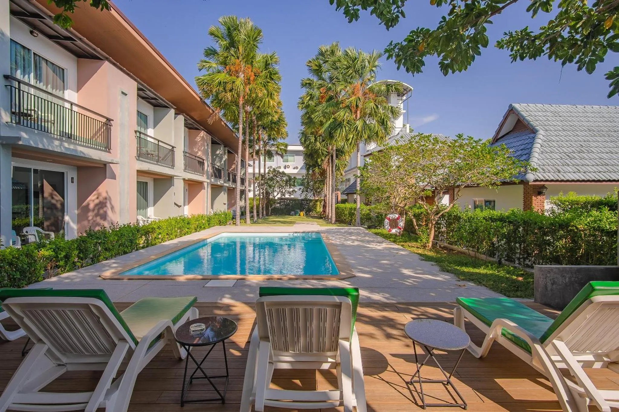 Transats verts alignés devant une piscine rectangulaire dans un jardin tropical.