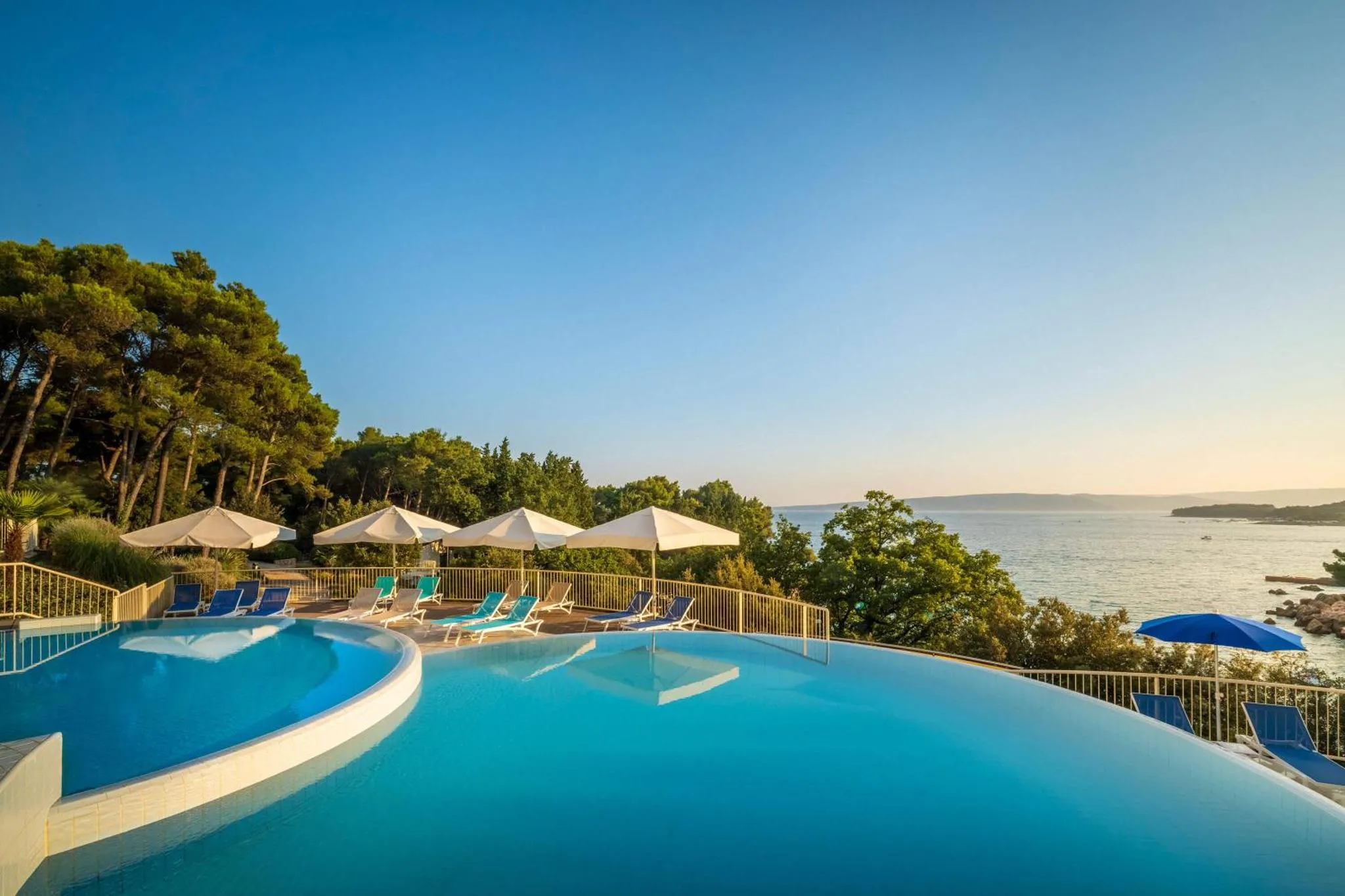 Piscine à débordement avec transats et parasols face à la mer.