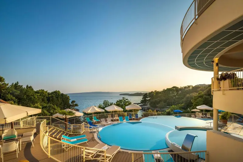 Terrasse avec piscine et transats en contrebas d'une végétation luxuriante.
