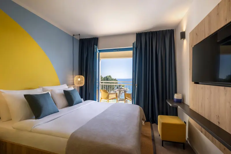 Une chambre lumineuse avec un grand lit donnant sur une vue mer.
