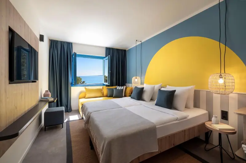 Chambre lumineuse avec un grand lit et un canapé face à la mer.