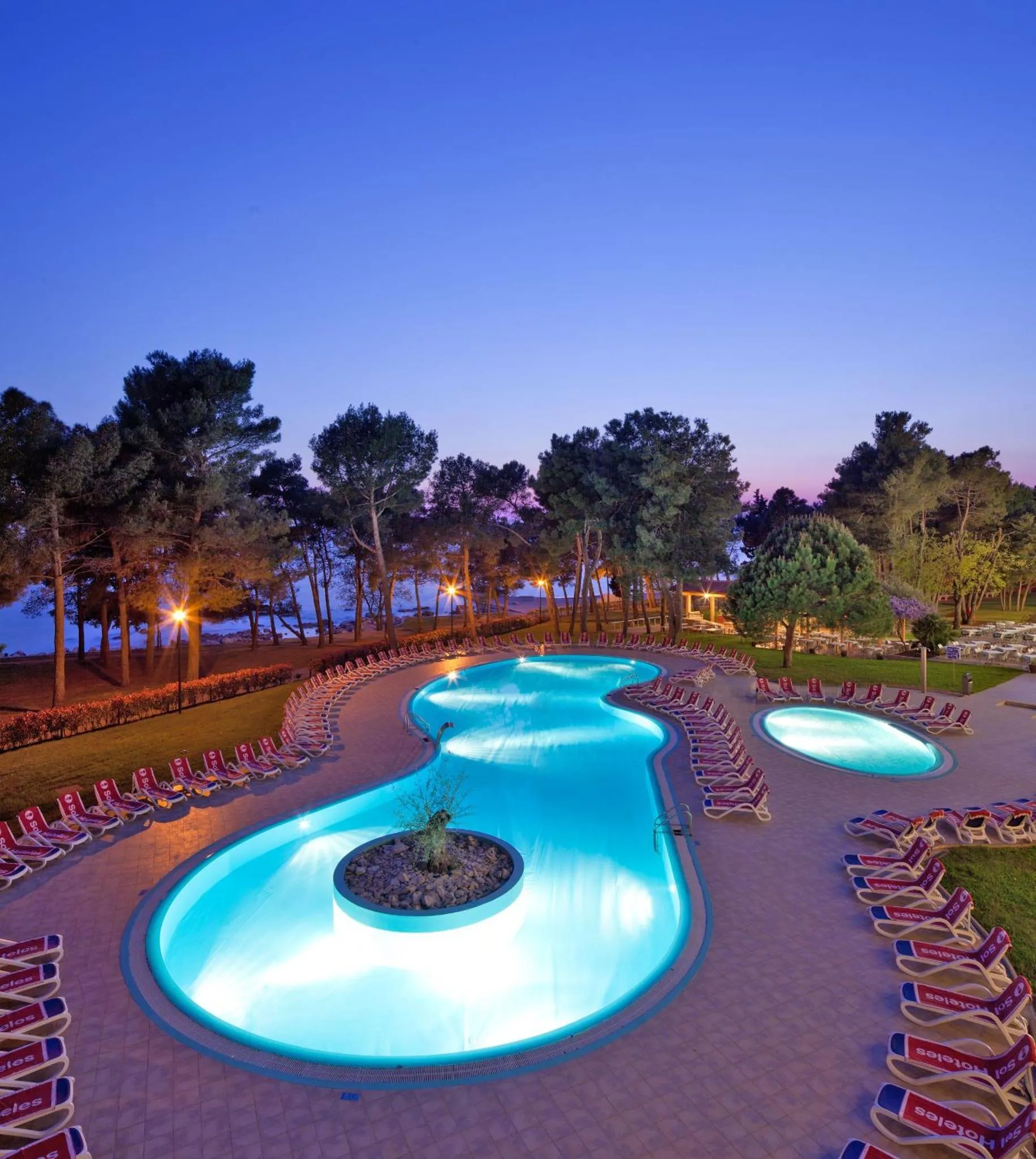 Piscine illuminée au crépuscule avec transats alignés.