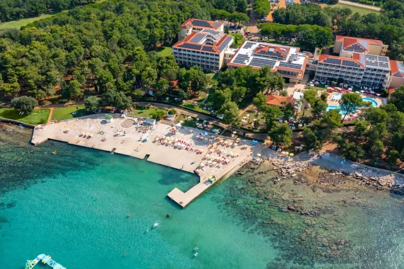 Vue aérienne d'un complexe hôtelier bordant une plage de sable et une côte rocheuse.