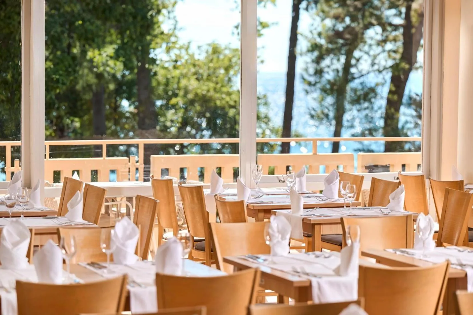Une salle de restaurant lumineuse avec des tables dressées et une vue sur la mer.