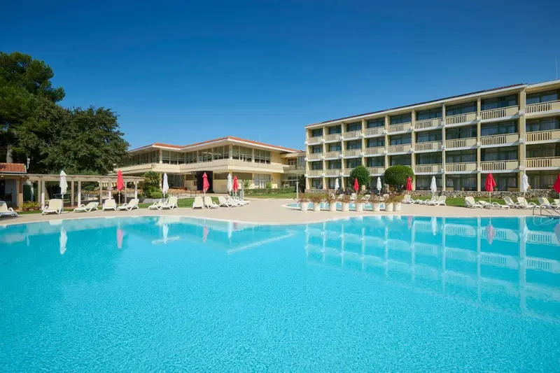 Vue d'une piscine turquoise devant un bâtiment beige à plusieurs étages.