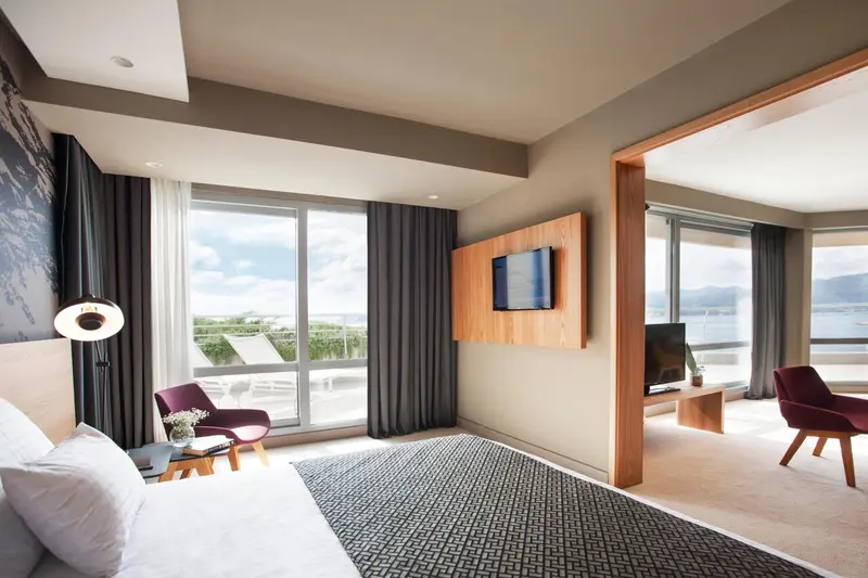 Chambre lumineuse avec un grand lit et un fauteuil près d'une fenêtre.