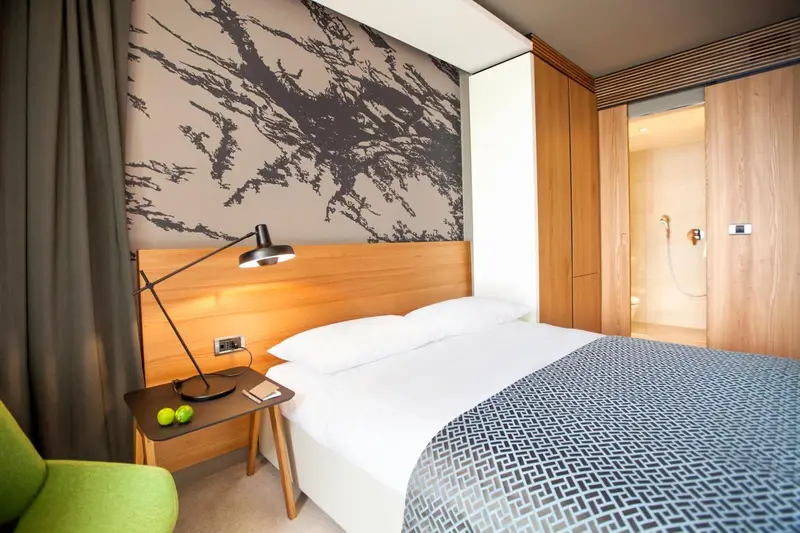 Une chambre lumineuse avec un lit fait et une décoration murale abstraite.