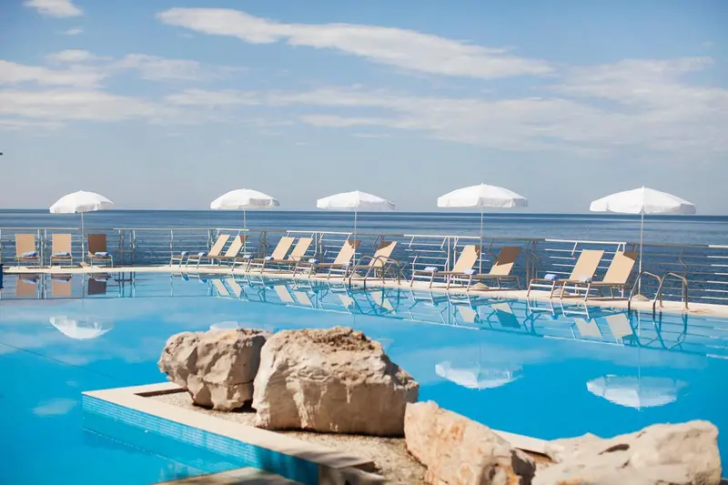 Transats blancs disposés autour d'une piscine bleue reflétant le ciel et la mer.