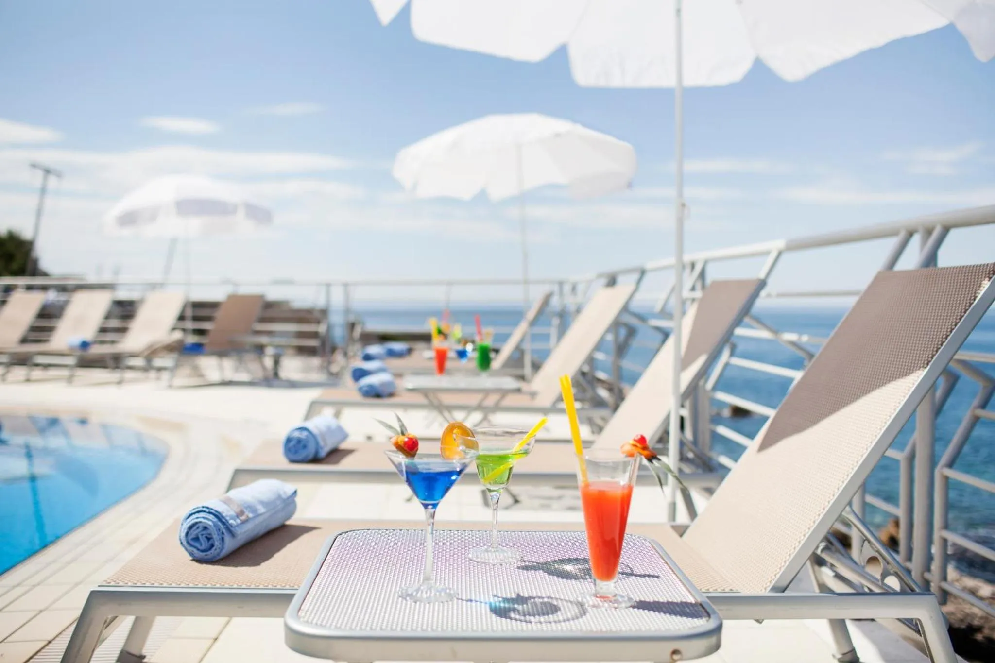 Transats et cocktails colorés au bord d'une piscine avec vue sur la mer.