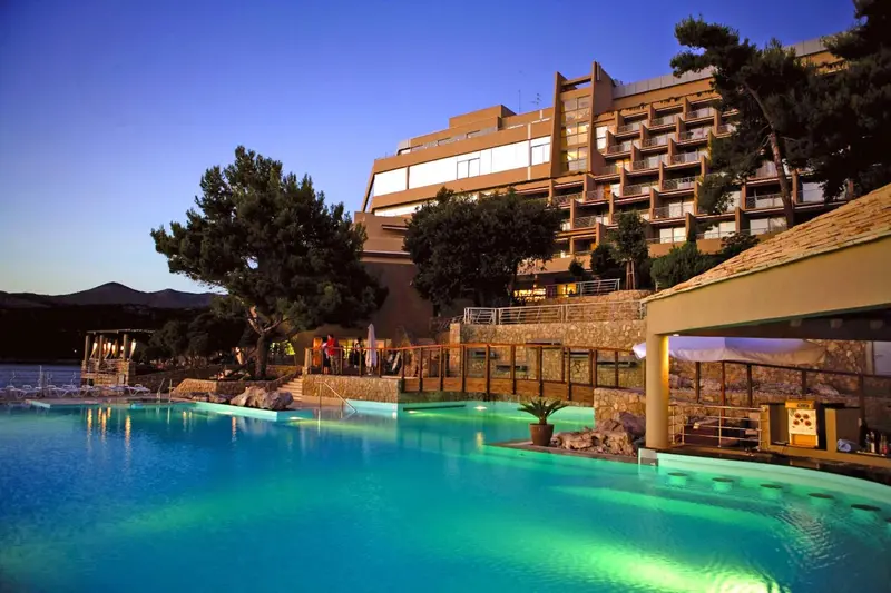 Bâtiment éclairé au bord d'une piscine turquoise en soirée.