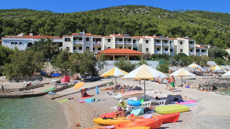 Baignade sur une plage de galets avec des transats et des kayaks.