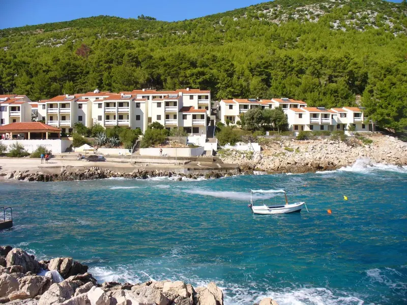 Bâtiment blanc avec des balcons surplombant une côte rocheuse et une mer bleue.