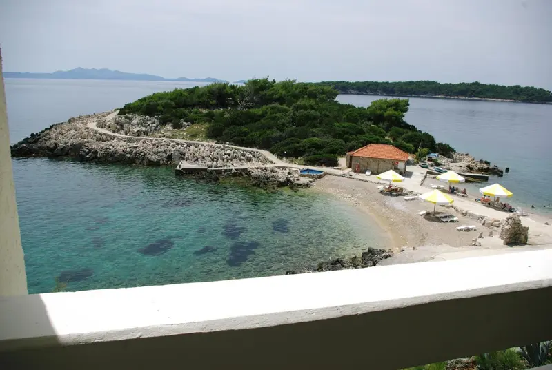 Une plage de galets bordée de parasols et de chaises longues surplombe une crique turquoise.