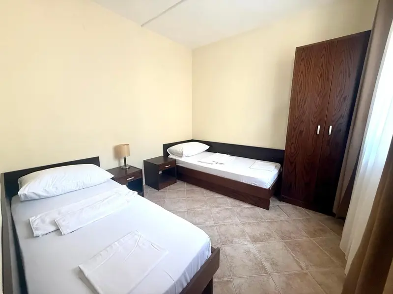 Une chambre lumineuse avec deux lits simples et une armoire en bois.
