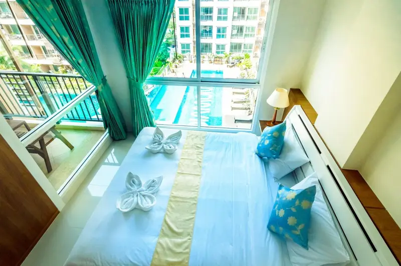 Une chambre lumineuse avec un lit décoré et une vue sur une piscine.