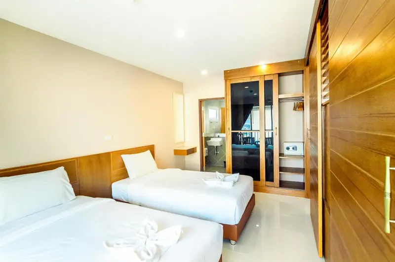 Une chambre lumineuse avec deux lits simples et un espace salon visible à travers une ouverture.