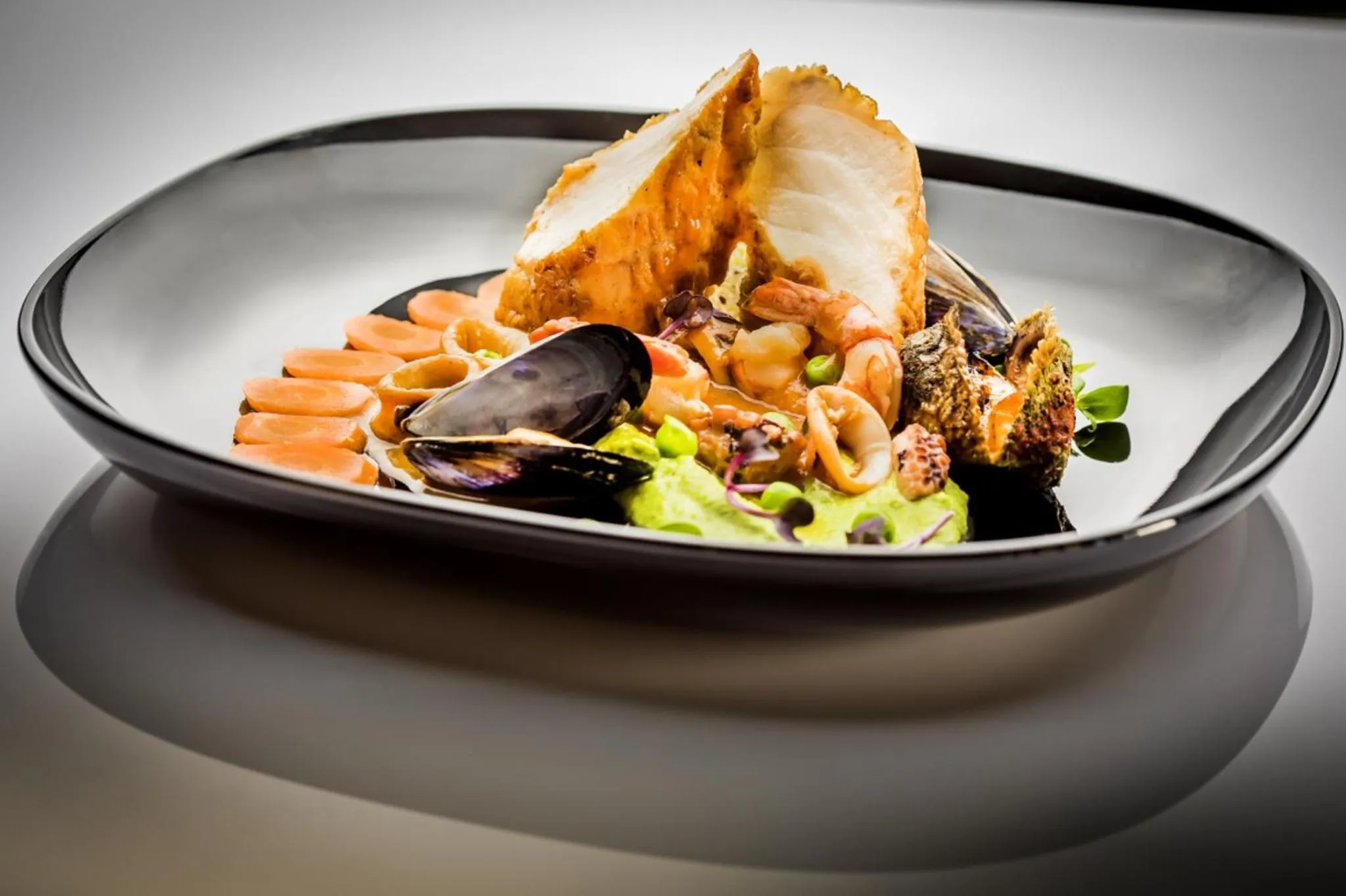 Assiette de poisson pané accompagnée de légumes et de fruits de mer.