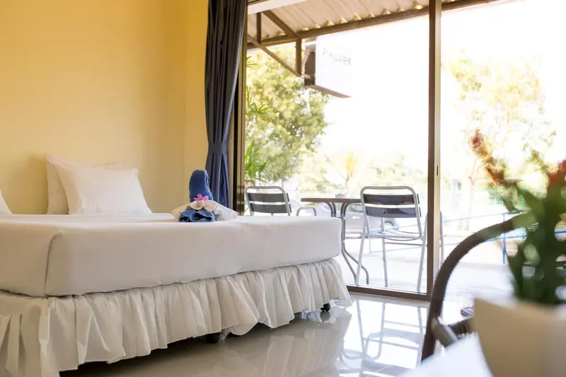 Une chambre lumineuse avec un lit recouvert de blanc et une terrasse accessible par une baie vitrée.