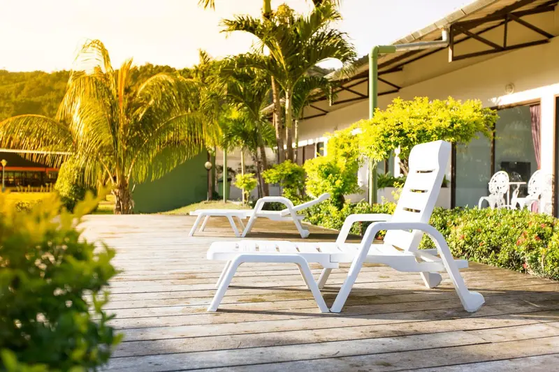 Transats blancs alignés sur une terrasse en bois ensoleillée, devant un bâtiment.