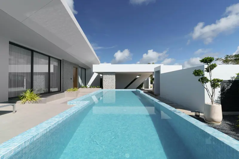 Une piscine rectangulaire turquoise est entourée d'une terrasse blanche et de bâtiments modernes.