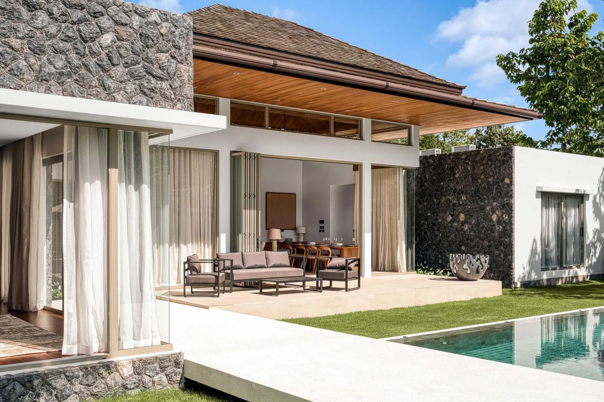 Terrasse ombragée avec salon et vue sur une piscine.