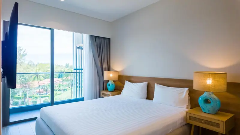 Chambre lumineuse avec un grand lit et vue sur la végétation.
