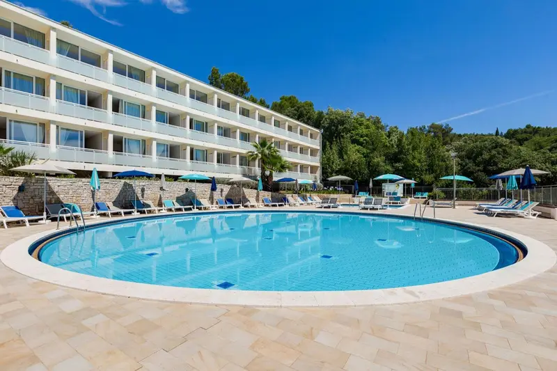Piscine circulaire au premier plan devant un bâtiment blanc à plusieurs étages.