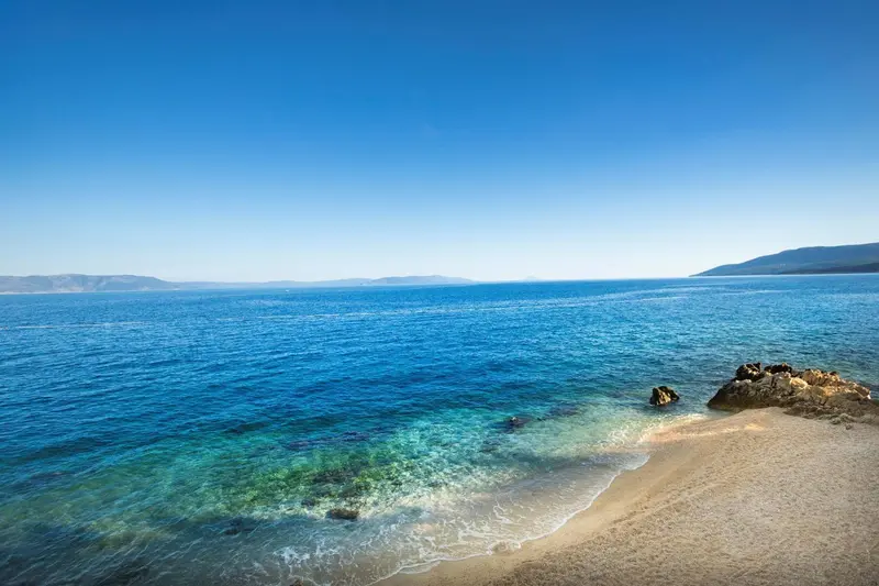 Une plage de sable fin borde une mer turquoise sous un ciel bleu dégagé.