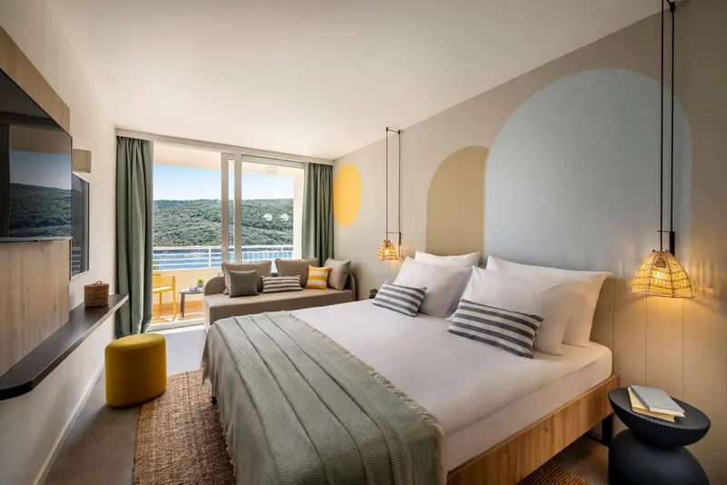 Une chambre lumineuse avec un grand lit et un canapé donnant sur une vue verdoyante.