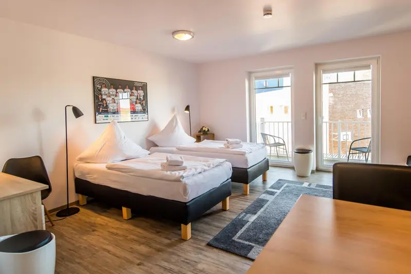 Une chambre lumineuse avec deux lits simples et un balcon.