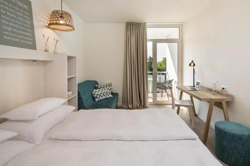 Une chambre lumineuse avec un lit simple et un coin lecture près d'une porte-fenêtre.