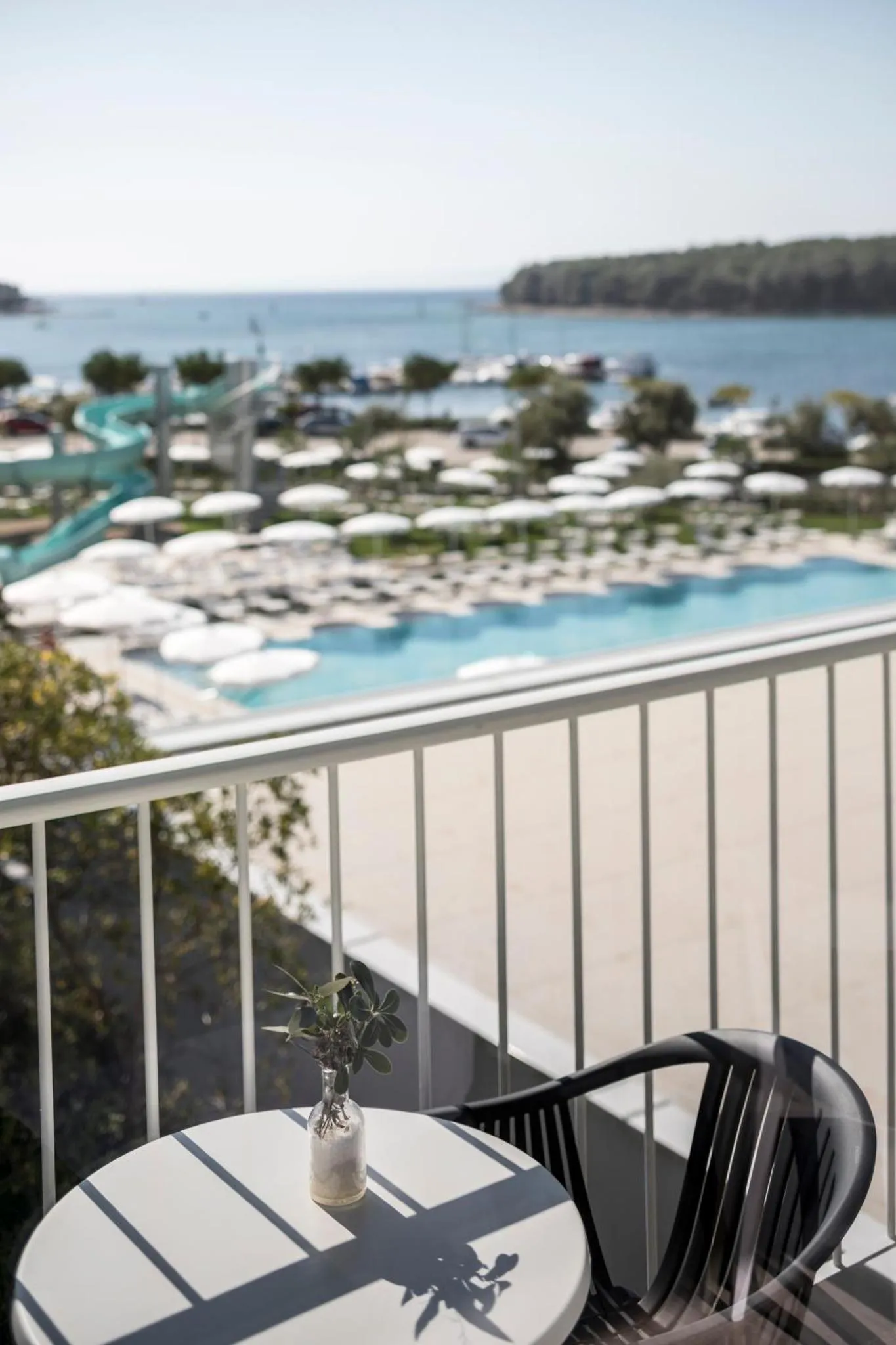 Une table et des chaises se trouvent sur un balcon avec vue sur la mer et une piscine.