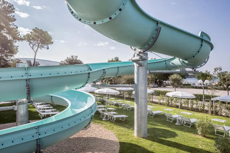 Toboggan aquatique turquoise se tordant au-dessus d'une pelouse verdoyante avec des transats et des parasols.