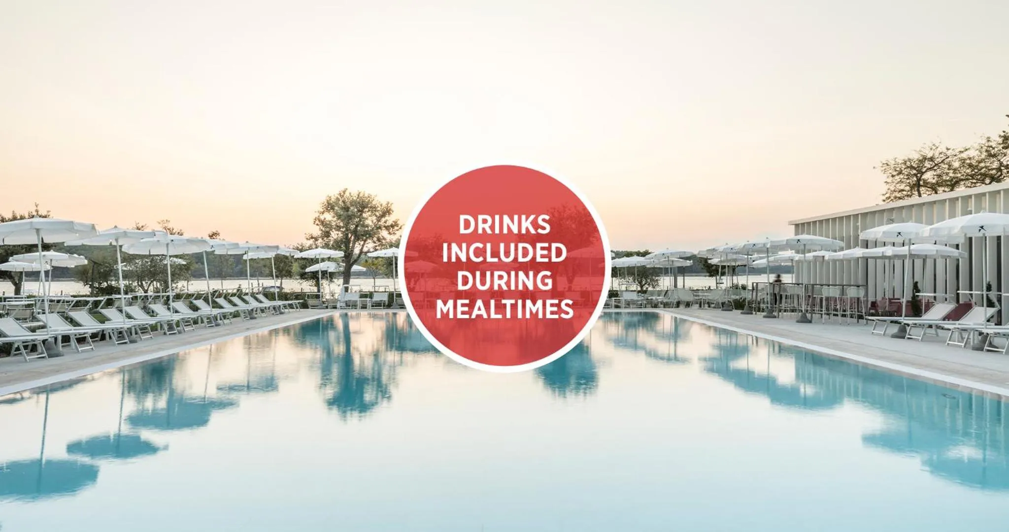 Une piscine rectangulaire bordée de transats blancs sous un ciel pastel.