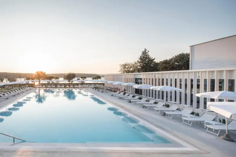 Une piscine rectangulaire bordée de transats blancs sous des parasols.