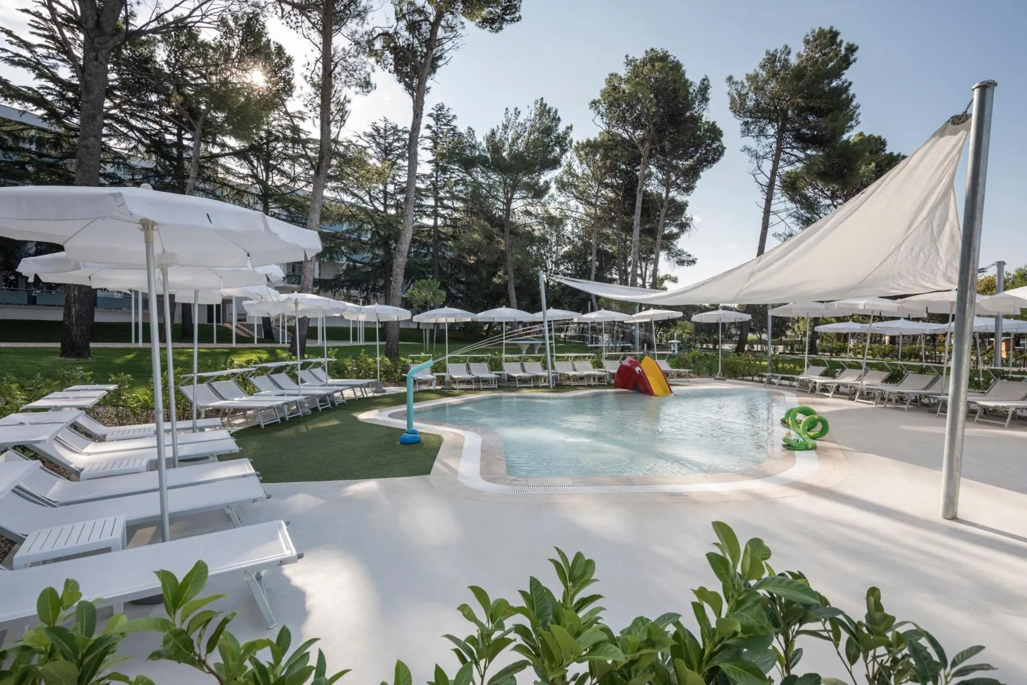 Transats blancs disposés autour d'une piscine ombragée par des parasols.
