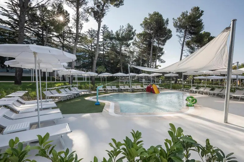 Transats blancs disposés autour d'une piscine ombragée par des parasols.