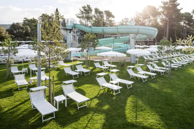 Transats blancs alignés sur une pelouse verte près d'une piscine avec toboggan.