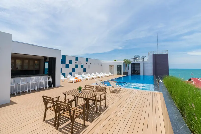 Terrasse avec transats et tables près d'une piscine à débordement.